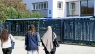 Une jeune fille portant le voile, accompagnée de plusieurs amies, devant l'entrée d'un lycée en France.