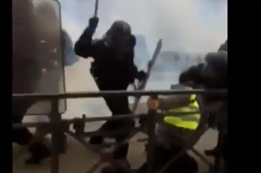 Le jeune homme se plaque sur la rambarde du pont et s'y accroche. Un gendarme le frappe alors avec une matraque sur le dos à au moins 9 reprises.