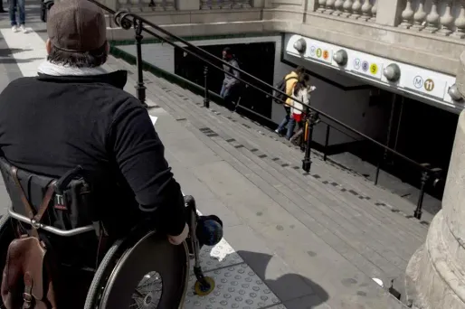 Une personne en situation de handicap devant l'escalier d'une bouche de métro