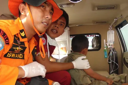 Deux sauveteurs aident un jeune survivant du naufrage.