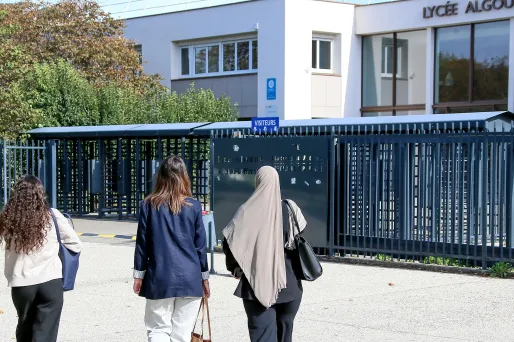 Une jeune fille portant le voile, accompagnée de plusieurs amies, devant l'entrée d'un lycée en France.